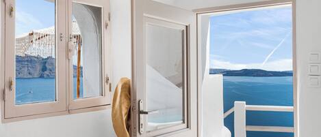 A room with a view of the sea, a white door, and a window with a view of a building.