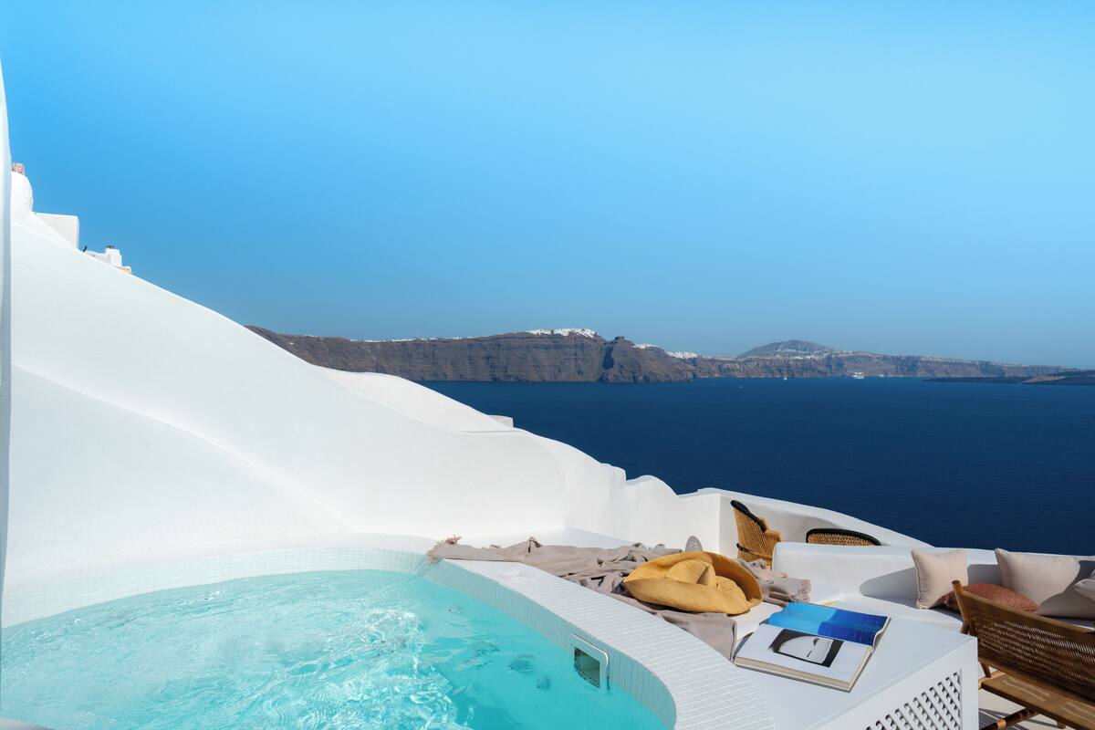 Un jacuzzi con vistas al mar y acantilados, paredes blancas y mobiliario de mimbre.