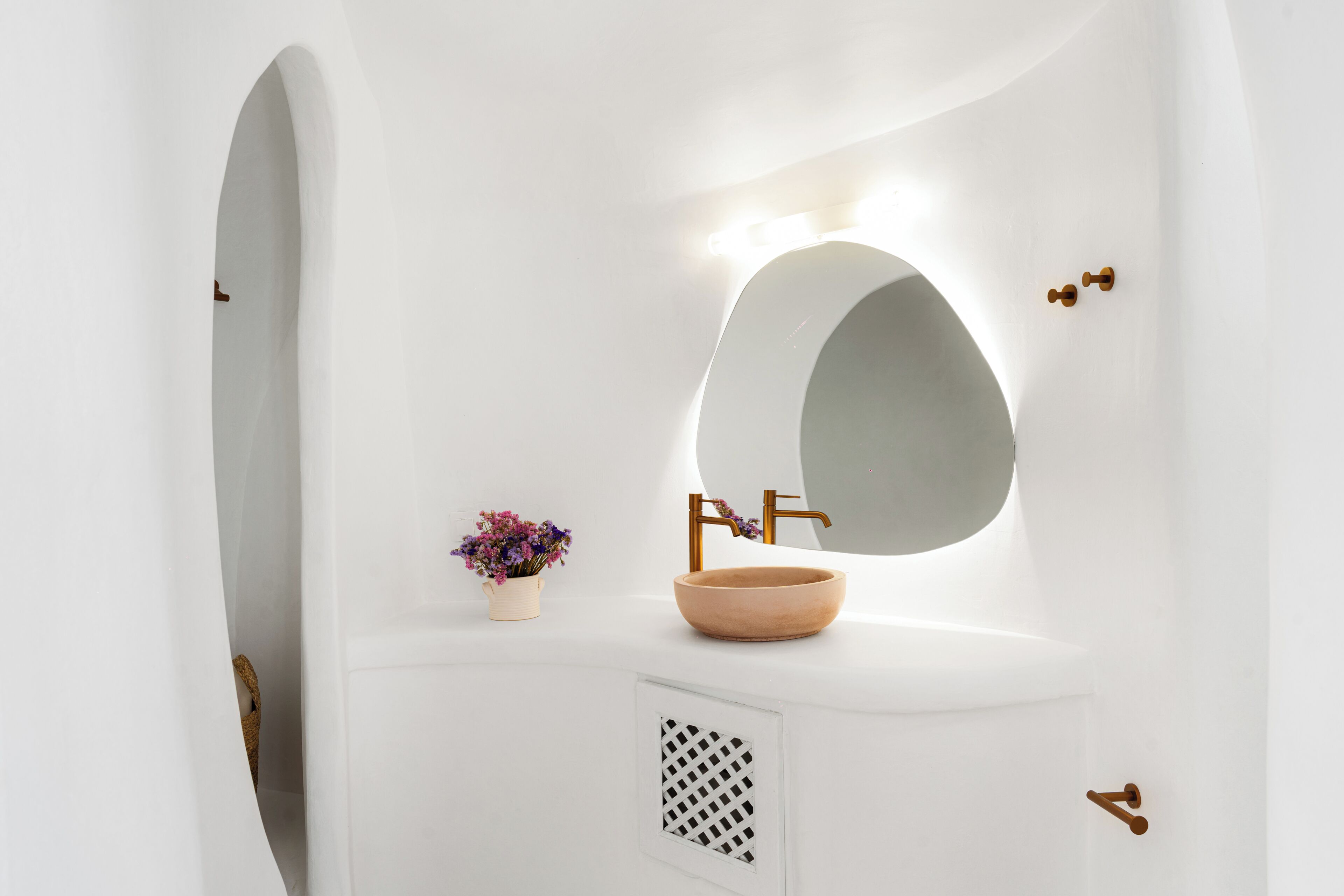A white bathroom vanity with a round mirror, a wooden bowl sink, and a small potted plant.