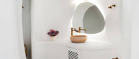 A white bathroom vanity with a round mirror, a wooden bowl sink, and a small potted plant.