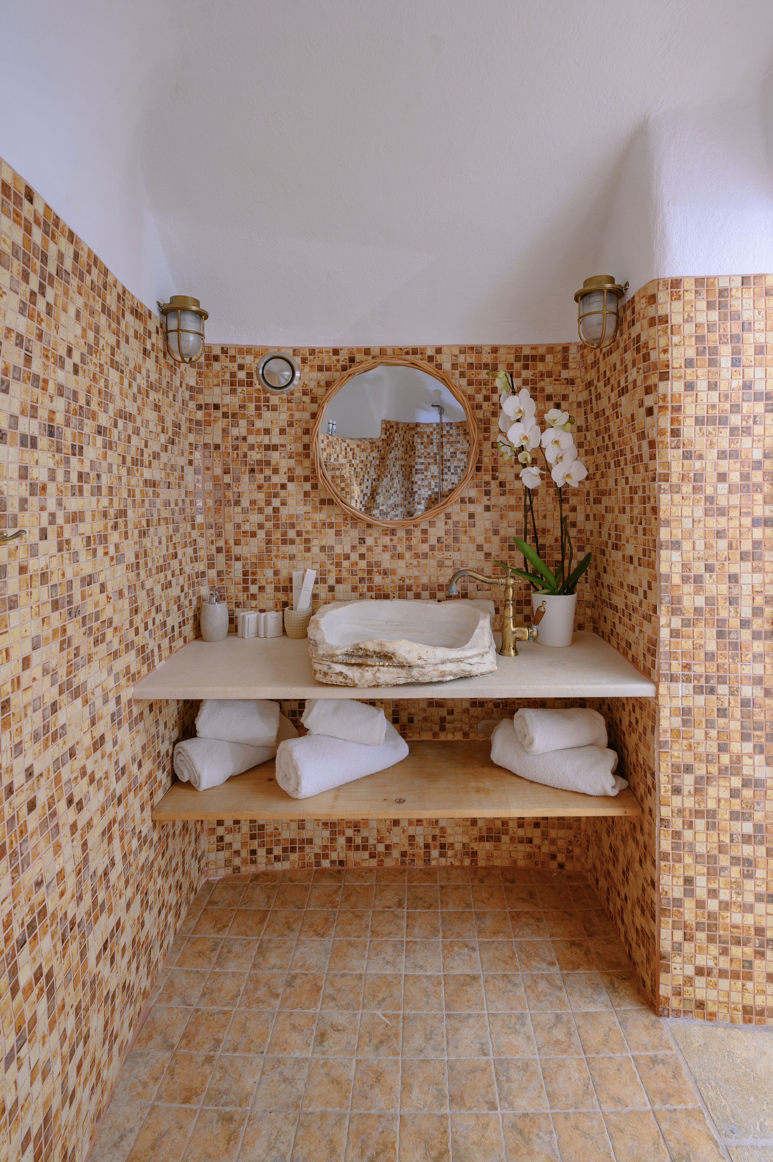 Un baño con paredes de mosaicos, un lavamanos con espejo y una repisa con toallas.