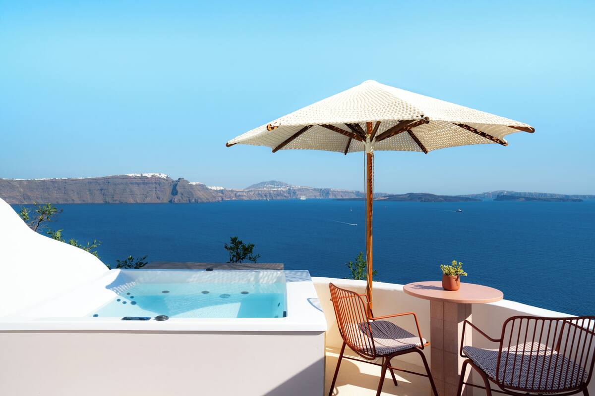 Balcón con hidromasaje, dos sillas, una mesa y una sombrilla con vista al mar.