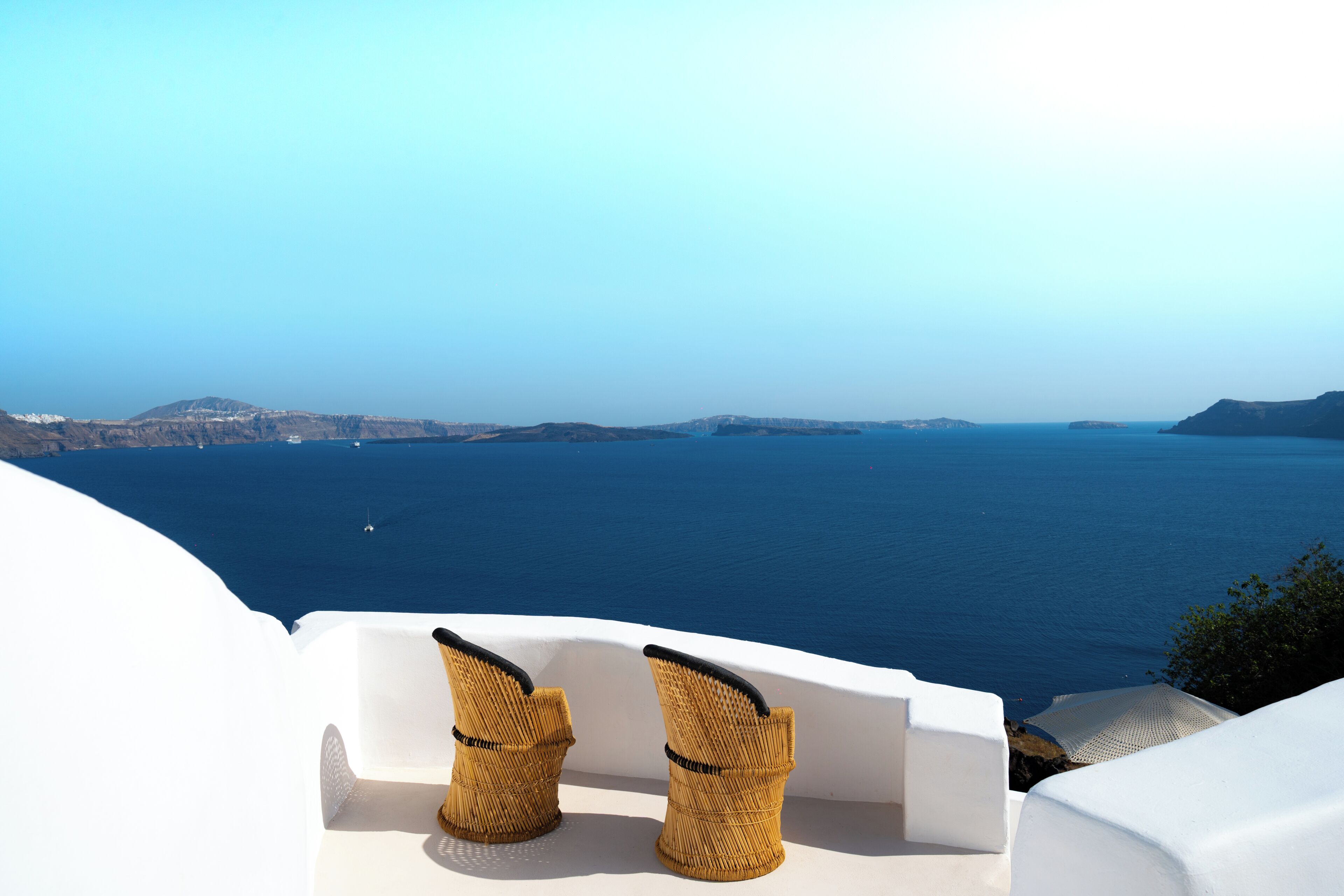A view of the sea from a white building with two wicker chairs.