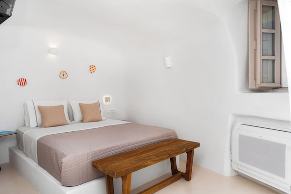 A bedroom with a bed, a wooden bench, a wall-mounted heater, and decorative wall lights.