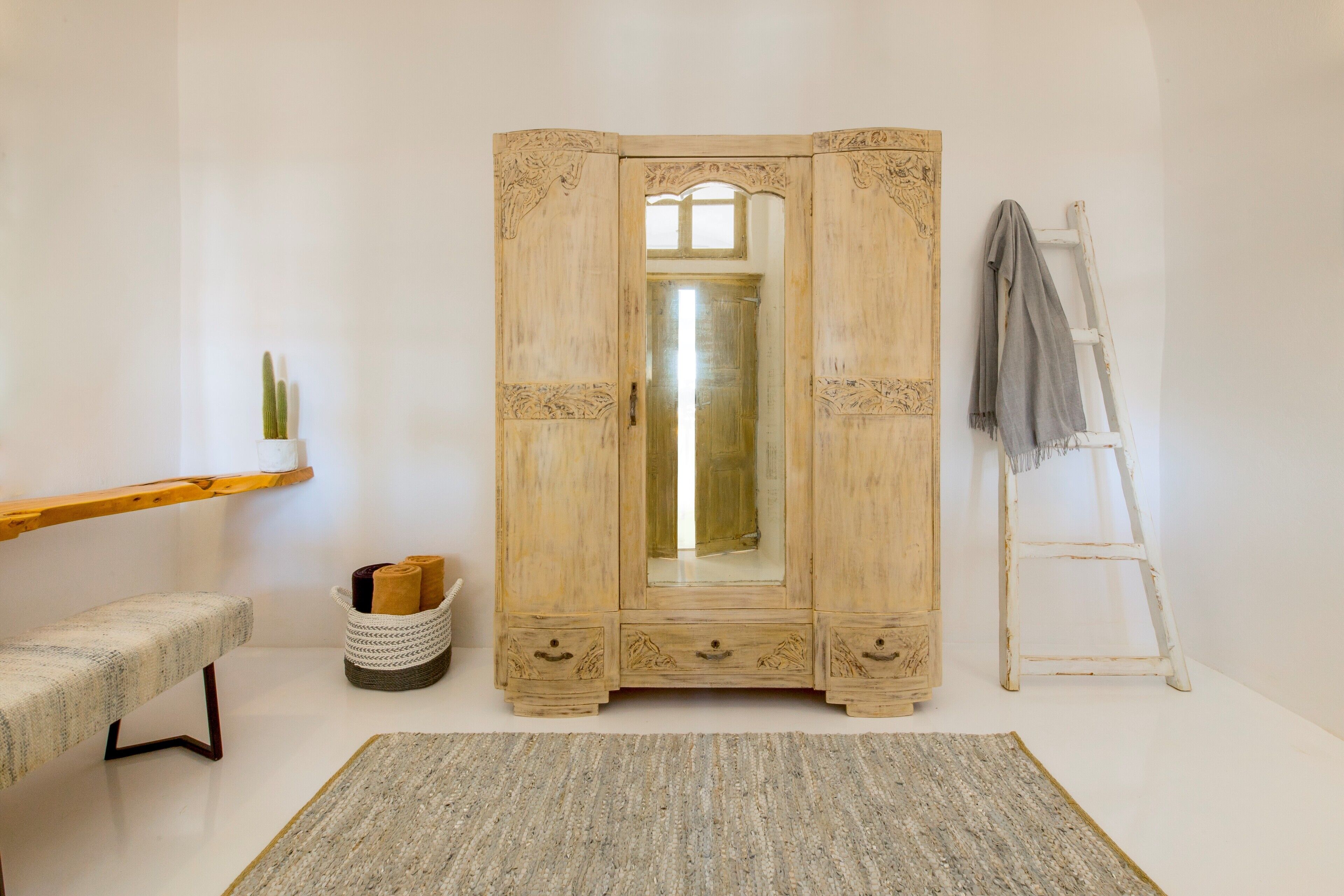 Una habitación con un armario de madera, un banco, una cesta tejida y una escalera.