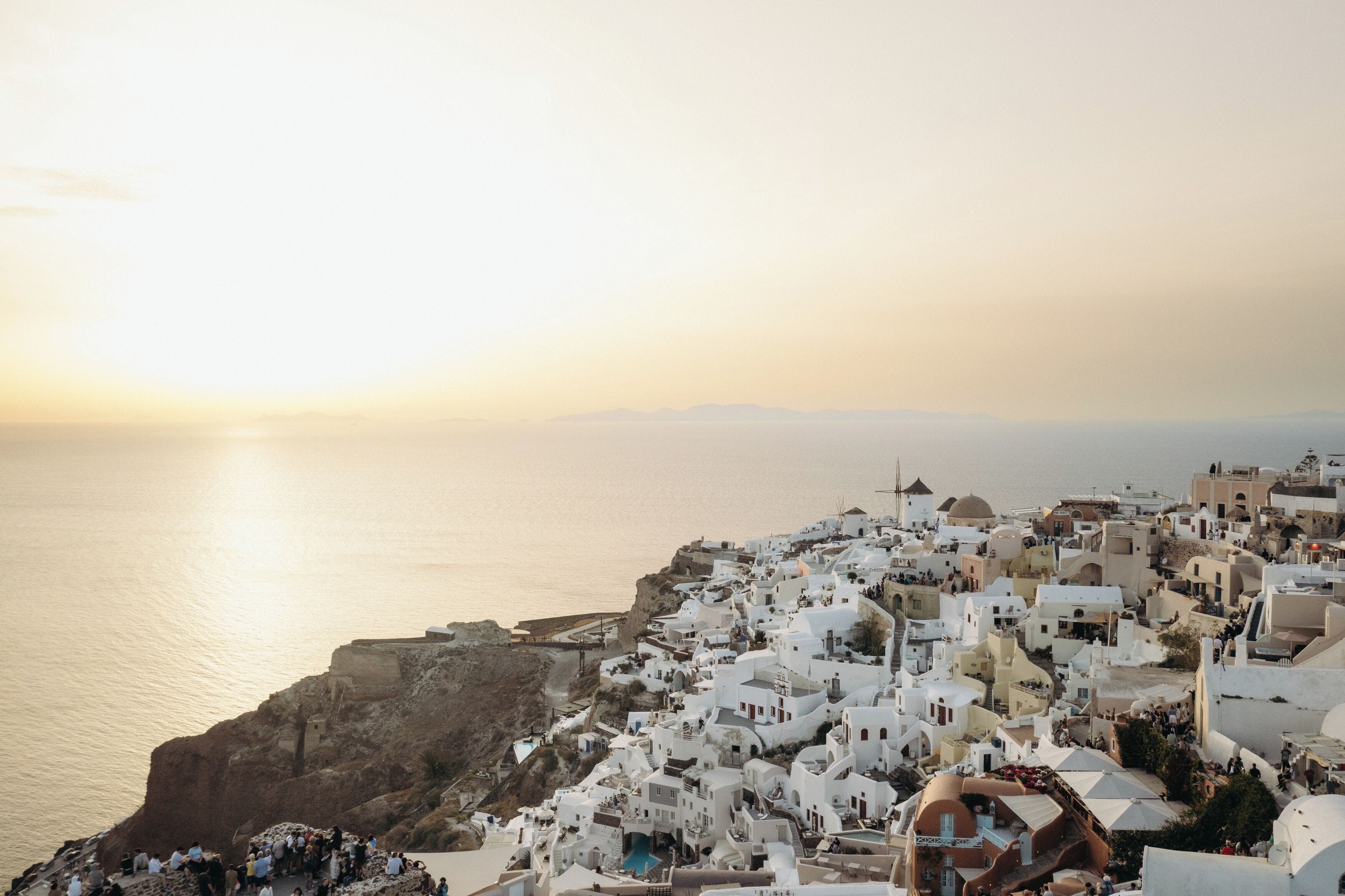 A coastal town with white buildings, a cliffside, and a view of the sea.