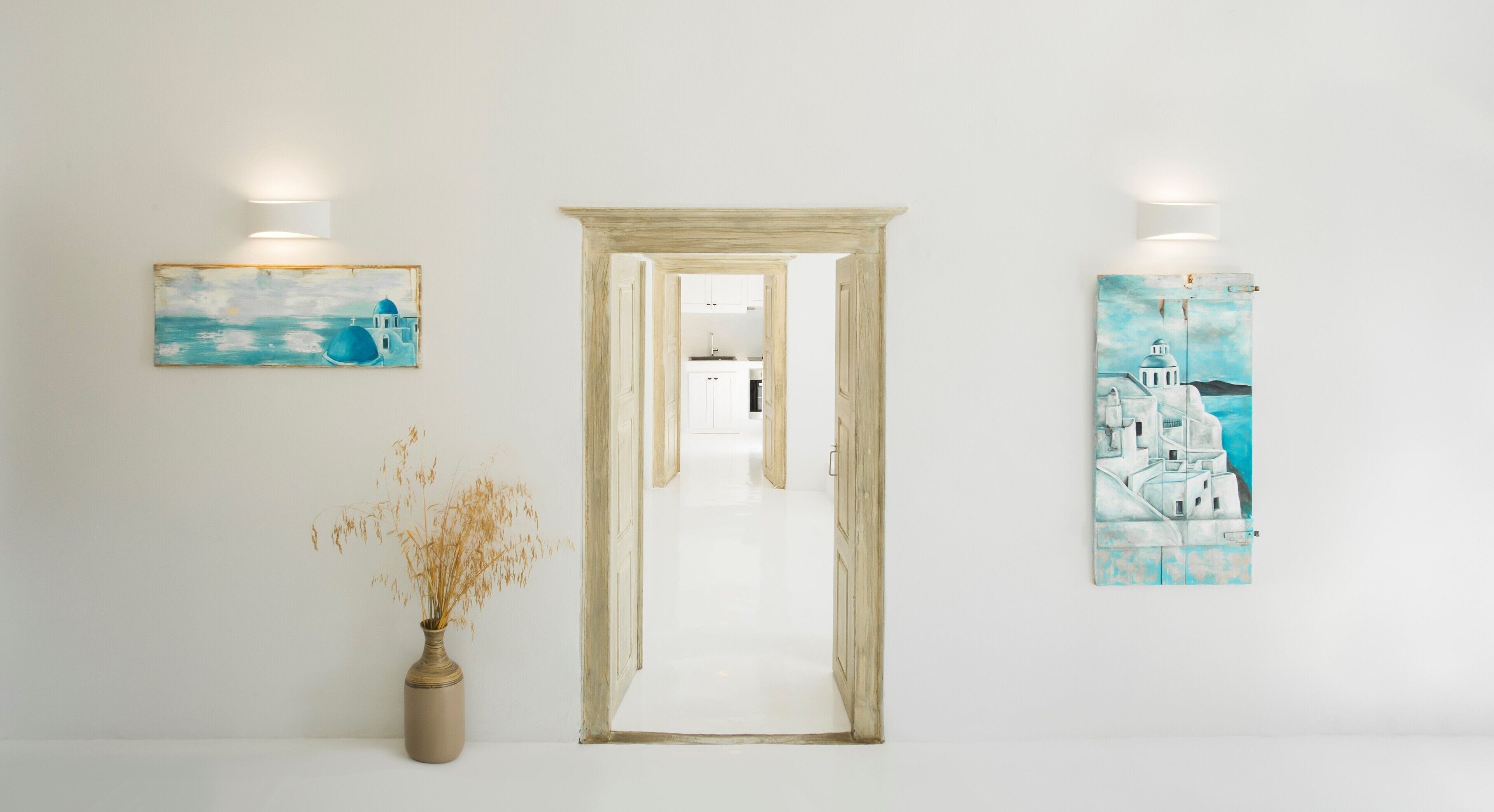 A hallway with a door leading to a kitchen area. There are two wall-mounted light fixtures on either side of the door.
