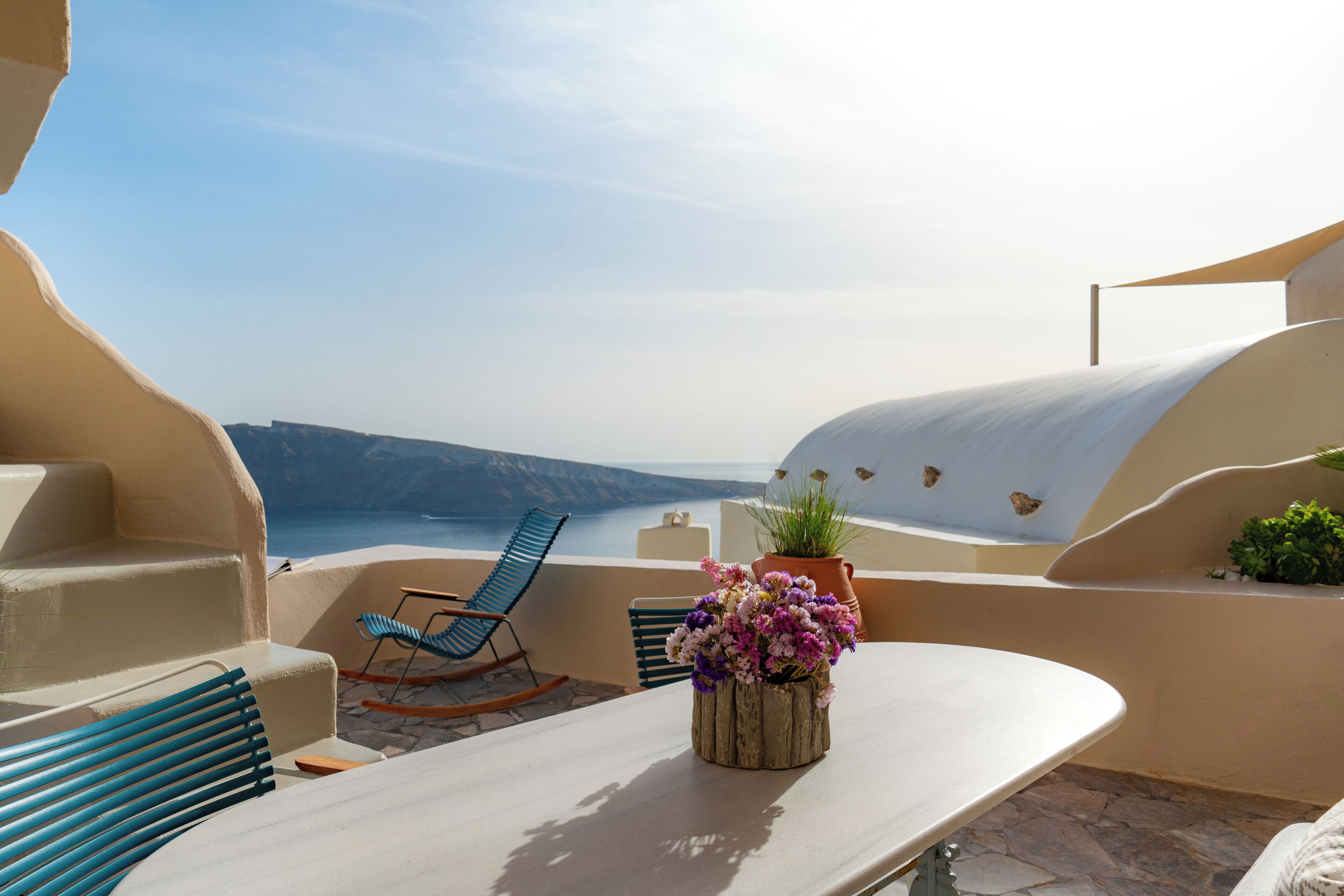 Een terras met een tafel, stoelen en een bloevas.