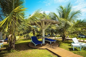 A tropical garden with palm trees, a gazebo, and lounge chairs. - Hotel Sarakawa (Lomé)