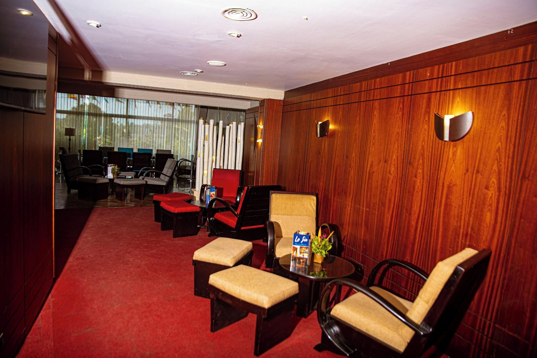 Habitación de hotel con alfombra roja, paneles de madera y un área de estar con sillas y una mesa.