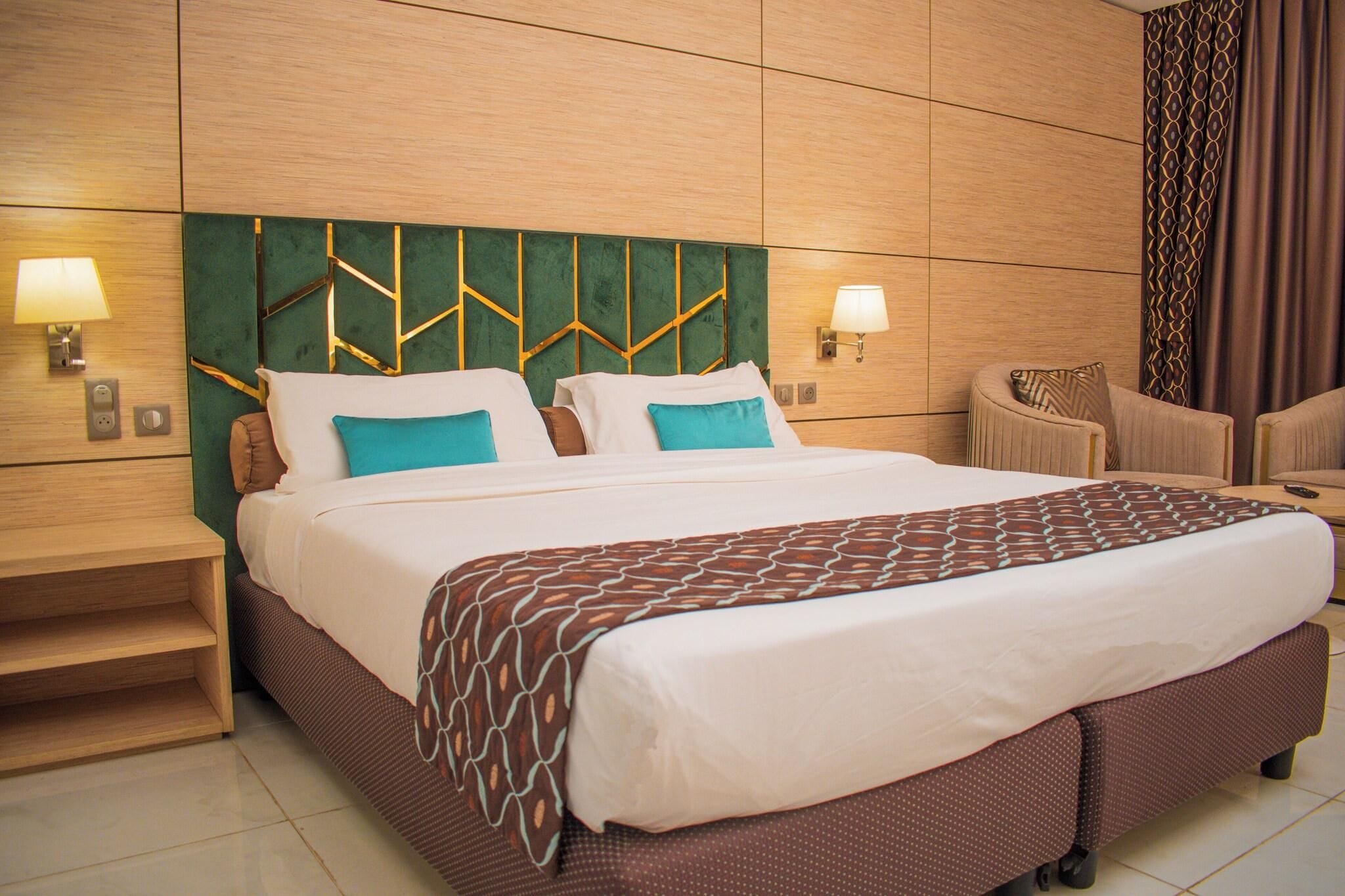 A hotel room with a large bed, two bedside tables, a chair, and a wall-mounted lamp.