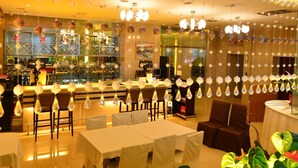Ein Restaurant mit Barbereich, Tischen mit weißen Tischdecken und hängenden Lampen.