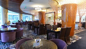 Ein Restaurant mit runden Tischen und violetten Stühlen, einem gemusterten Teppich und einer Wand mit hängenden Dekorationen.