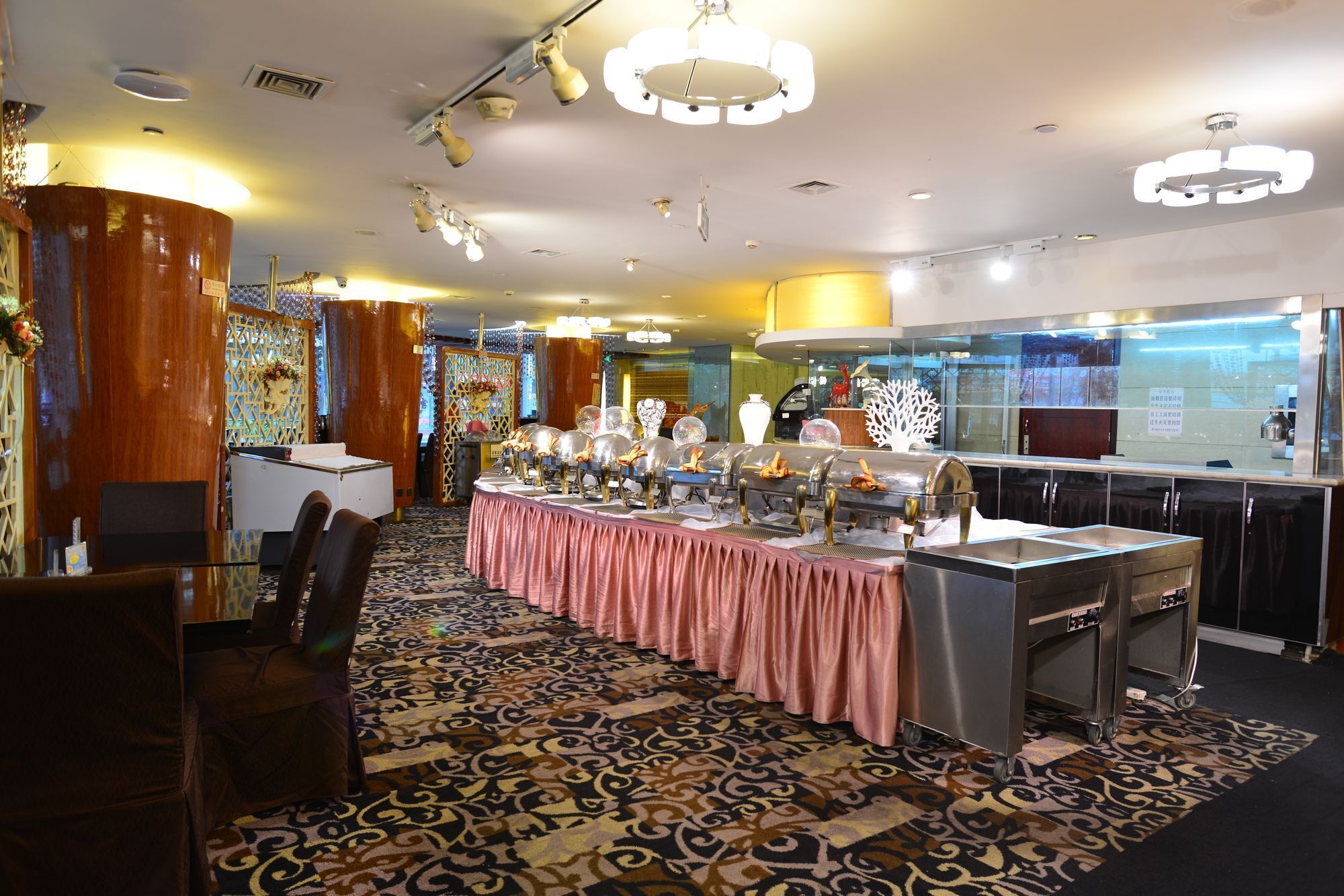 A banquet hall with a long table covered in a pink tablecloth, surrounded by buffet stations with various food items.