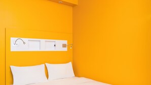 Een bed met wit beddengoed, een wit hoofdbord en een wit wandplankje met een handdoek en een lamp.