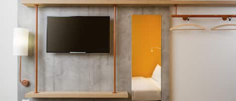Una habitación moderna con un televisor de pantalla plana montado en una pared gris, un estante de madera debajo, una mesita de noche y una lámpara colgante.