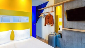 Een hotelkamer met een bed, een televisie, een kapstok met een jas en een koffer.