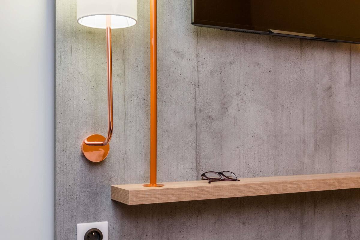 A modern room with a concrete wall, a mounted television, a wooden shelf, a floor lamp, and a wall socket.