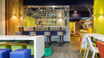 Een modern restaurantinterieur met hoge tafels, kleurrijke stoelen en een decoratieve wand.