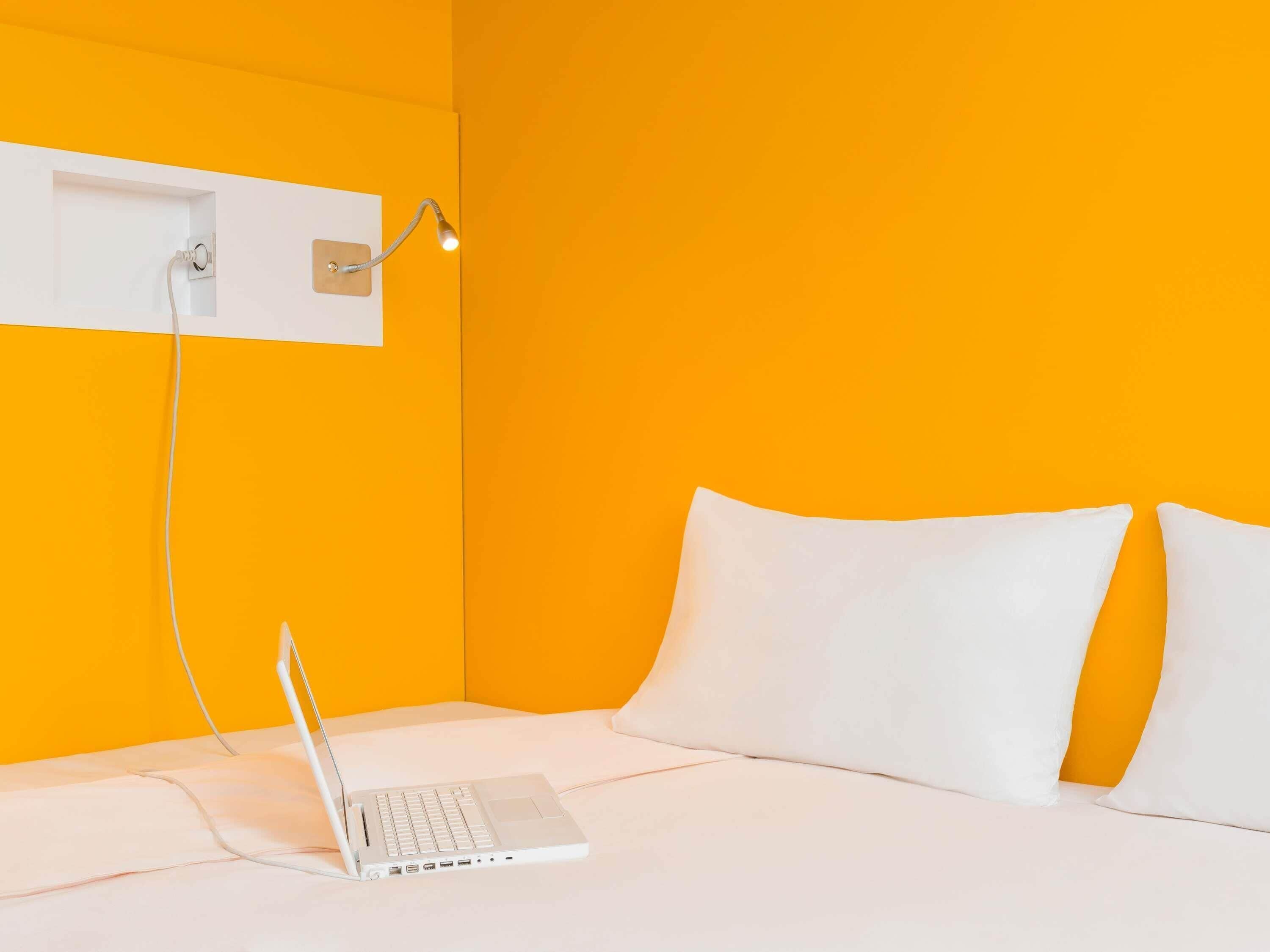 Ein Zimmer mit einem Bett, einem Laptop auf dem Bett und einer Wandleuchte.