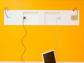 Ein weißes Regal mit zwei Wandlampen und einem Tablet an einer gelben Wand.
