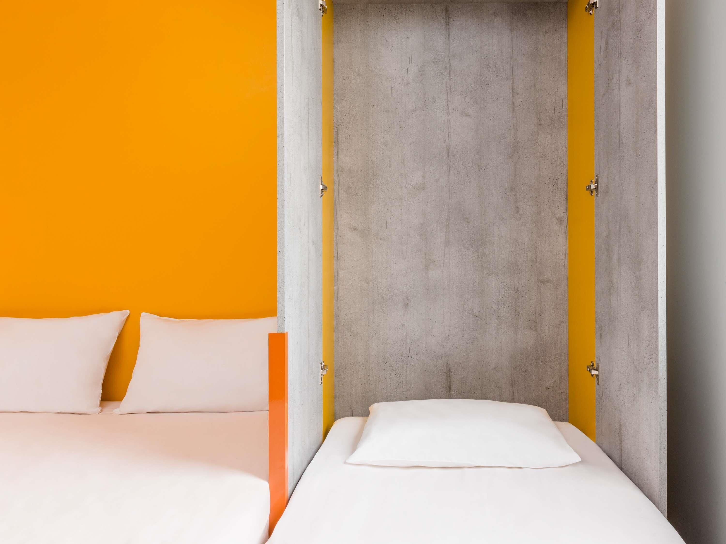 Een kamer met een bed, twee kussens en een betonnen muur.