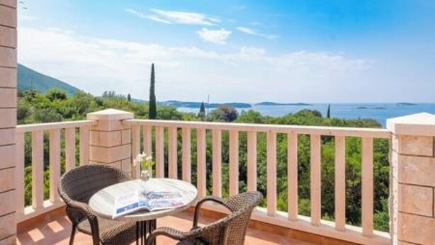 A balcony with a table and chairs, overlooking a scenic view of the sea and greenery. - Villa Panorama (Zupa dubrovacka)