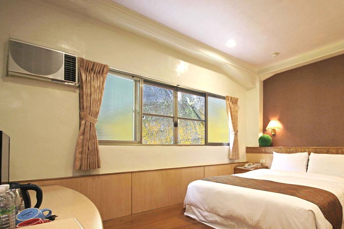 A hotel room with a bed, a desk, a lamp, and a window with curtains.