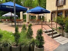 An outdoor patio area with blue umbrellas labeled 'Tucher,' stone steps, and potted plants.