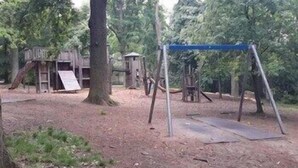 Un terrain de jeux avec des balançoires et un toboggan, entouré d’arbres.