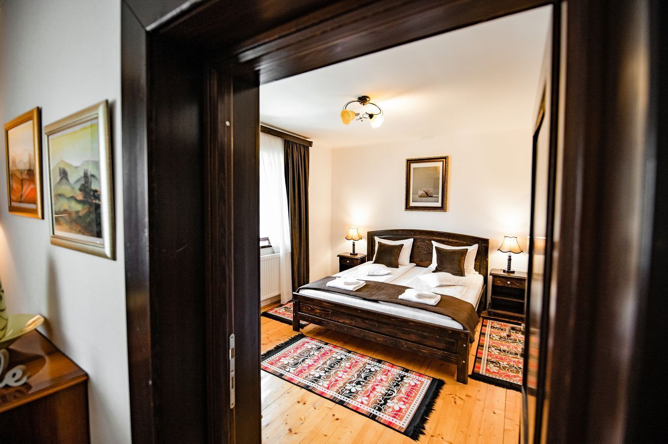 A bedroom with a wooden bed, two bedside tables with lamps, a patterned rug, and a framed picture on the wall.