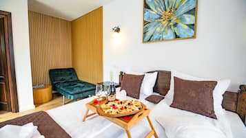 Quarto de hotel com cama, bandeja de madeira com petiscos, uma garrafa de champanhe e uma poltrona de descanso.