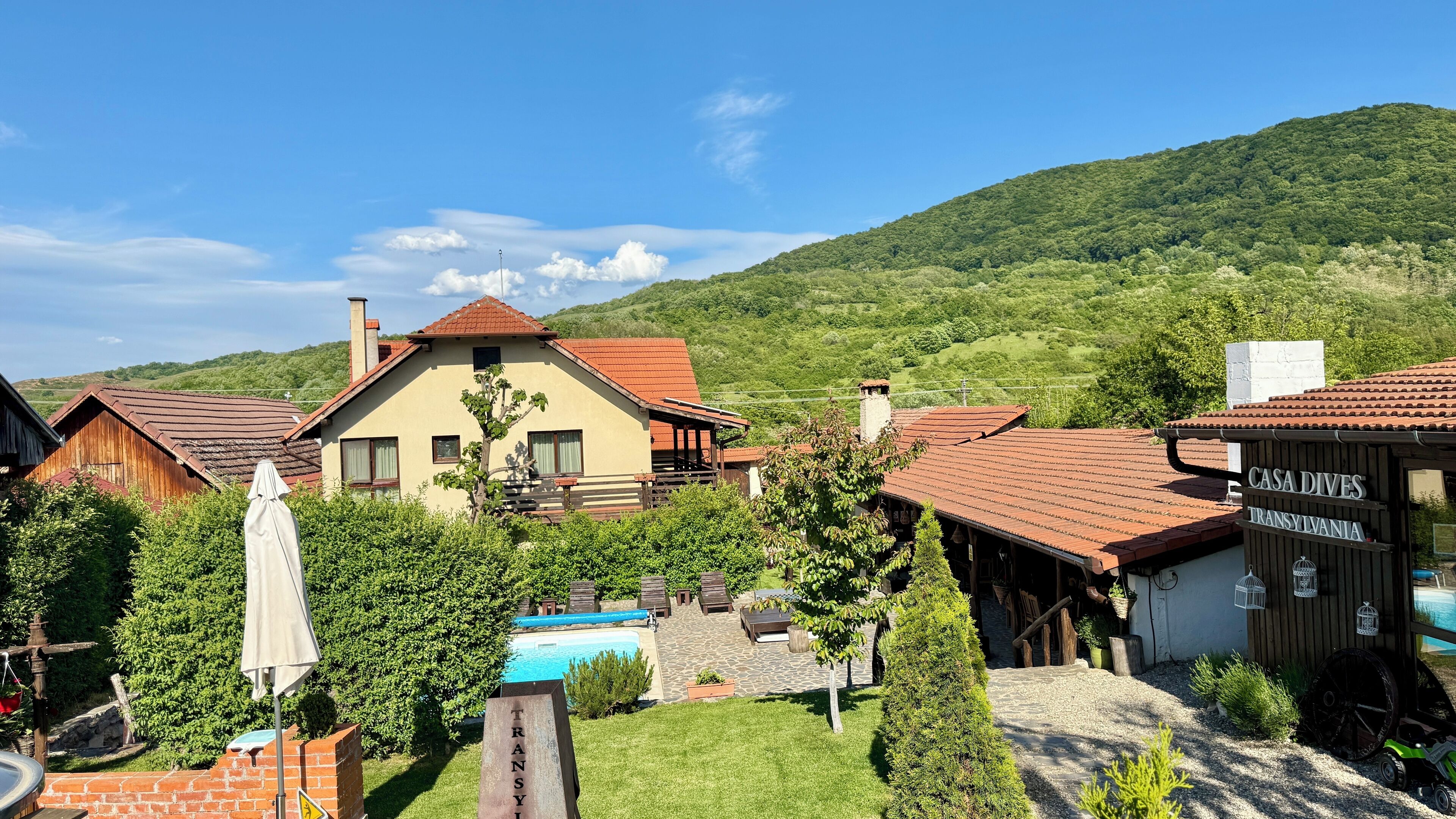 A rustic mountain lodge with a swimming pool, wooden cabins, and a sign for 'CASA DIVES Transylvania'.