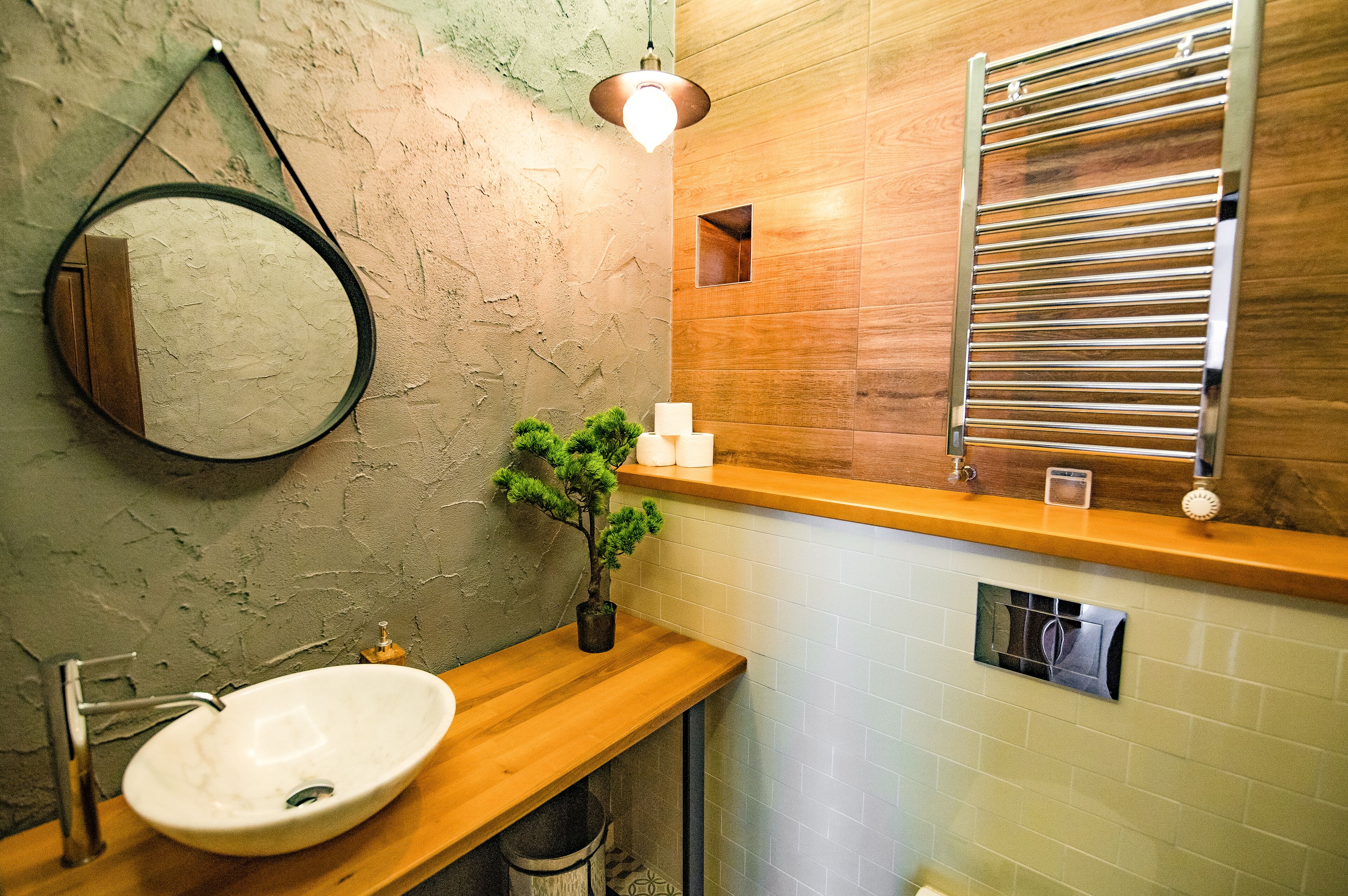 Une salle de bain avec un meuble-lavabo en bois, un miroir rond, une plante en pot et un porte-serviettes.