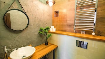 Une salle de bain avec un meuble-lavabo en bois, un miroir rond, une plante en pot et un porte-serviettes.