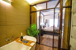 A modern bathroom with a bathtub, a wooden tray with a bottle and glass, and a green plant.