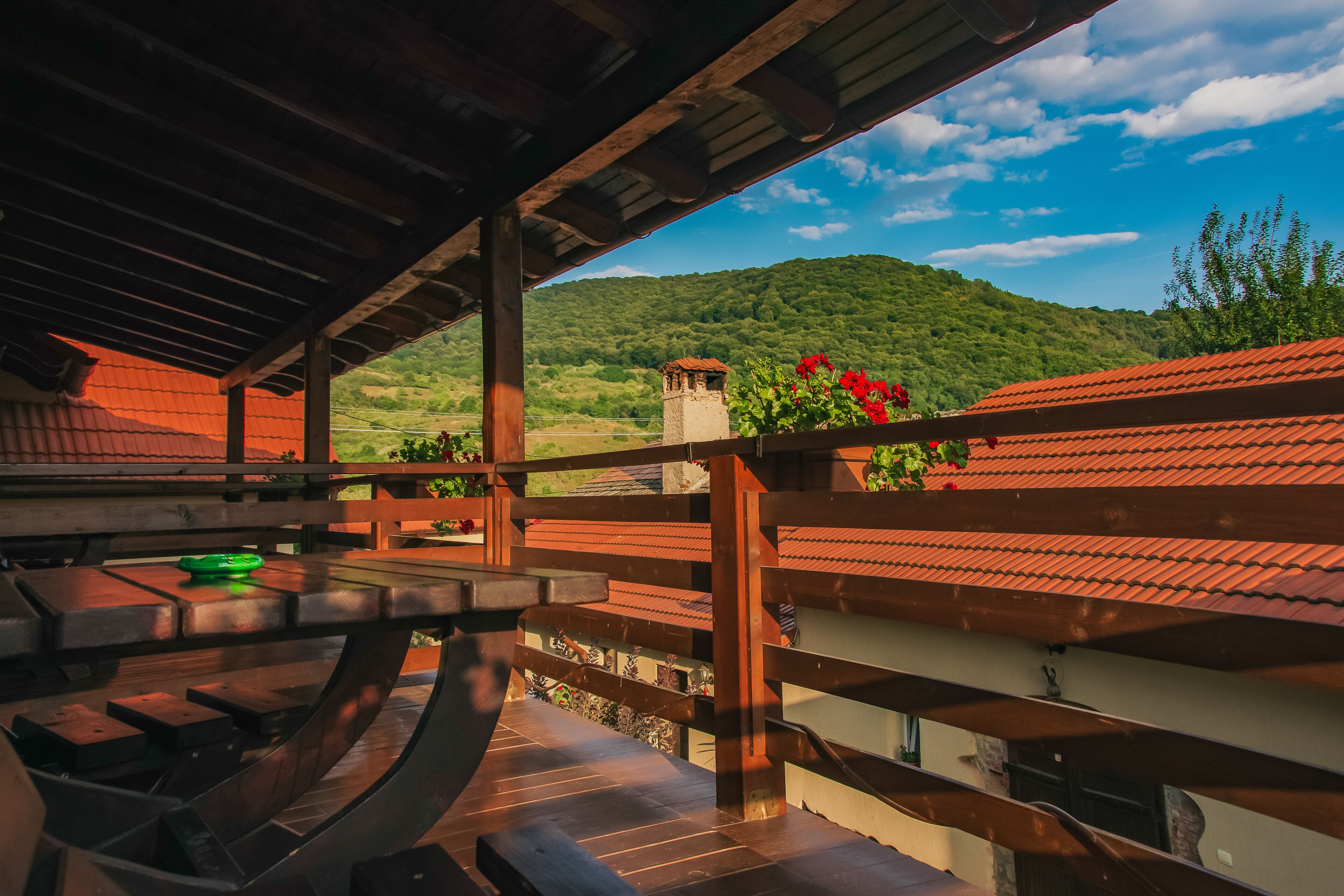 A covered outdoor area with a wooden deck, a table, and a view of a mountain.