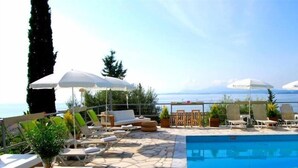 Zona junto a la piscina con sillones de descanso, sombrillas y vistas al mar.