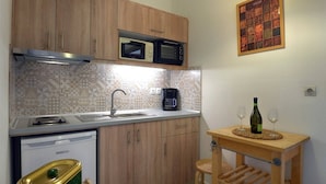 Cocina compacta con armarios de madera, microondas, cafetera y una pequeña mesa con copas de vino y una botella.