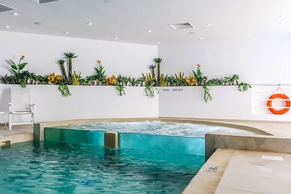 Un espace piscine avec une zone à eau claire, un mur blanc orné de plantes et un cercle de sauvetage sur la droite.
