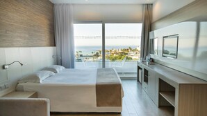 Een hotelkamer met een bed, een televisie, een bureau en een balkon met uitzicht op zee.