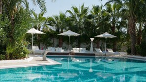 Une piscine entourée de palmiers, avec des chaises longues et des parasols.