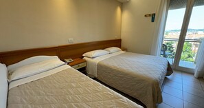 A hotel room with two beds, a nightstand, and a view of the city through a balcony door.