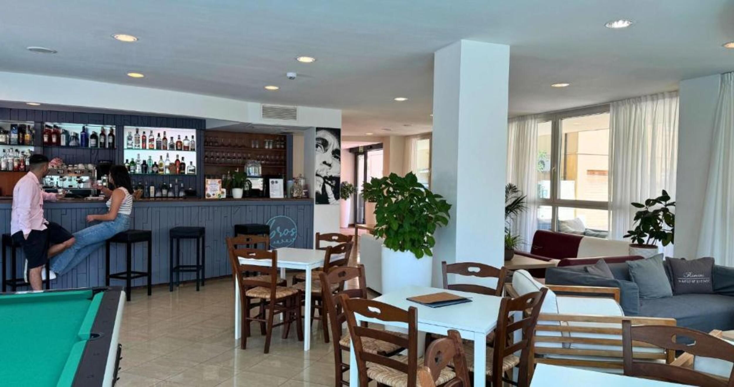Zona de bar con mesa de billar, asientos y barra con varias botellas.