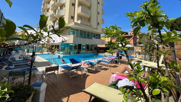 A hotel with a swimming pool, sun loungers, and a multi-story building. - Apogeo (Rimini)
