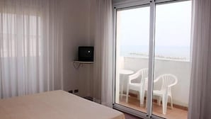 Hotellihuone, jossa on sänky, hyllyllä oleva televisio ja tuoleilla varustettu parveke.