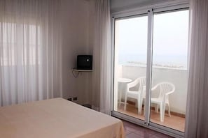 Une chambre d’hôtel avec un lit, un téléviseur posé sur une étagère et un balcon avec des chaises.