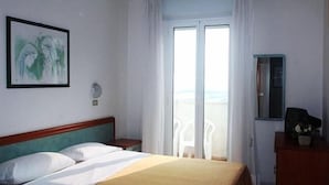 Hotellihuone, jossa on sänky, yöpöytä, lipasto, ikkuna verhoilla ja näkymä ulos.