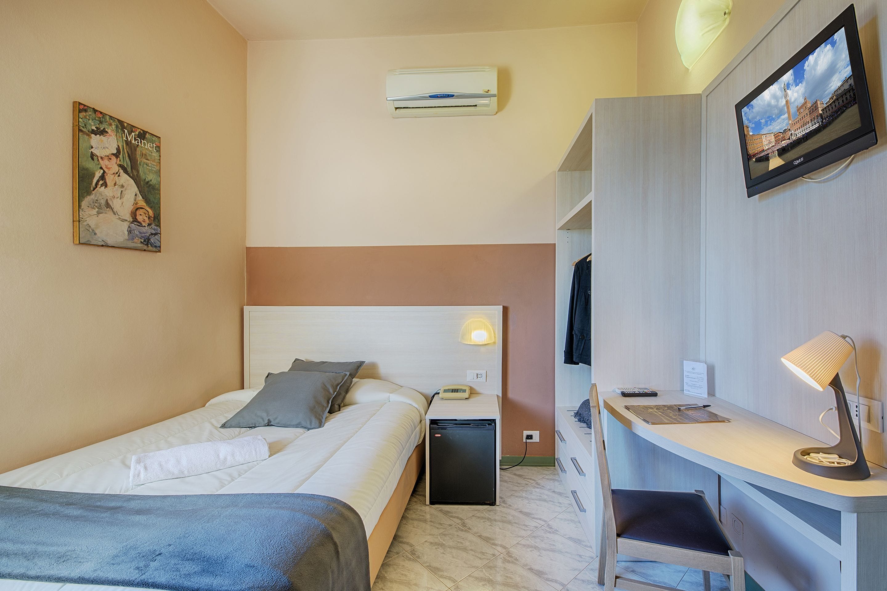 Ein Hotelzimmer mit einem Bett, einem Schreibtisch, einem Sessel, einem Fernseher, einer Klimaanlage und einem Bild an der Wand.