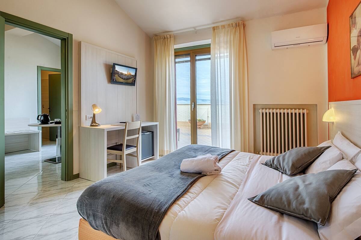 A hotel room with a bed, a desk, and a view of the sea.